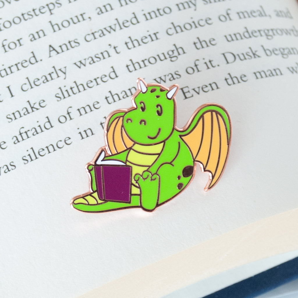 Mythical green and yellow dragon sitting and reading a book enamel pin