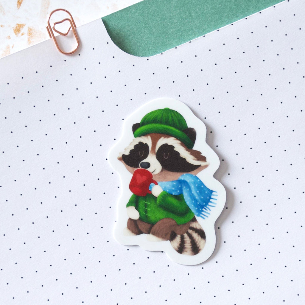 Fun Raccoon wearing a toque and scarf drinking cocoa vinyl sticker