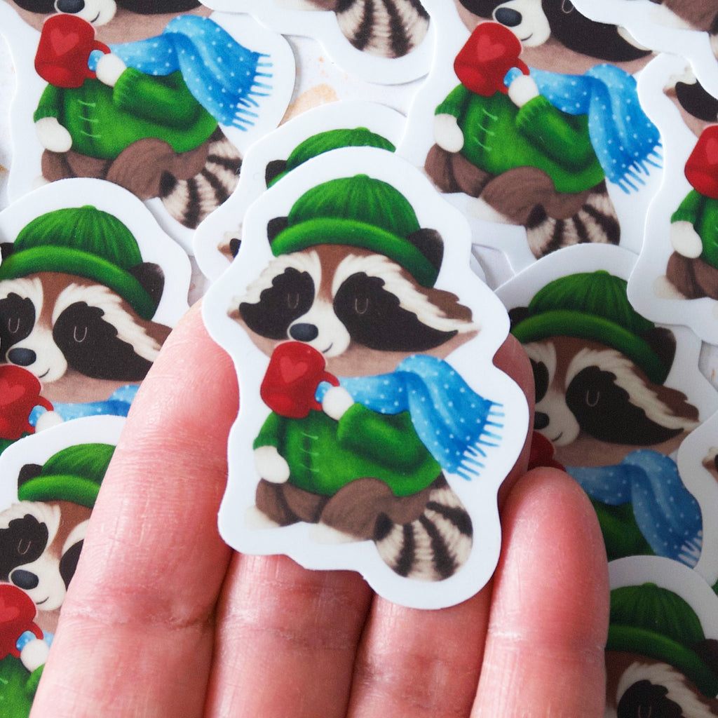 Fun Raccoon wearing a toque and scarf drinking cocoa vinyl sticker