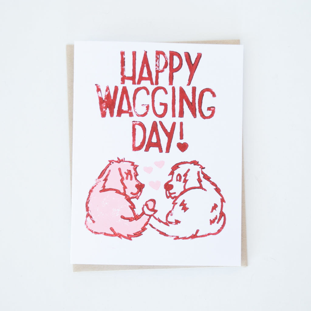 Two dogs with tails intertwined in red and pink with words "Happy Wagging day!" card