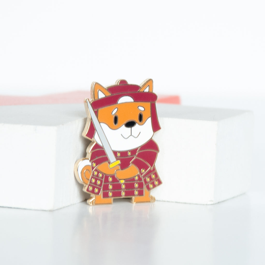 Japanese shiba dog wearing a red warrior's outfit wielding a sword enamel pin