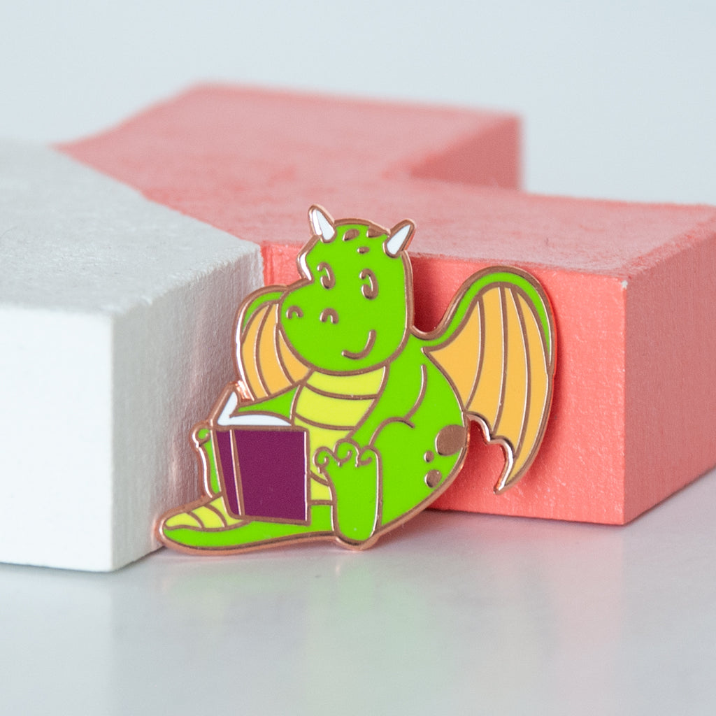Mythical green and yellow dragon reading a book enamel pin