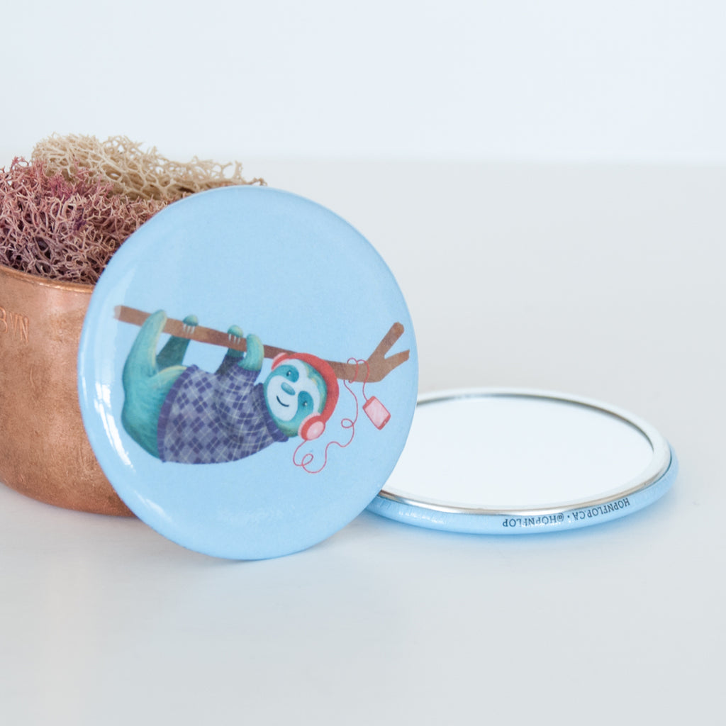 Sloth listing to music and hanging off a branch on a blue background illustrated travel pocket mirror